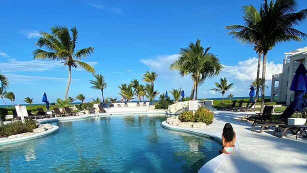 A pool area with lounge chairs, palm trees, and a view of the ocean.