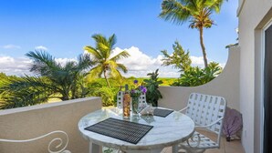 A round table with two chairs on a balcony, surrounded by palm trees and a clear sky.