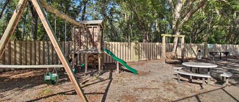 Ein Spielplatz mit Schaukeln, einer Rutsche und Picknicktischen.
