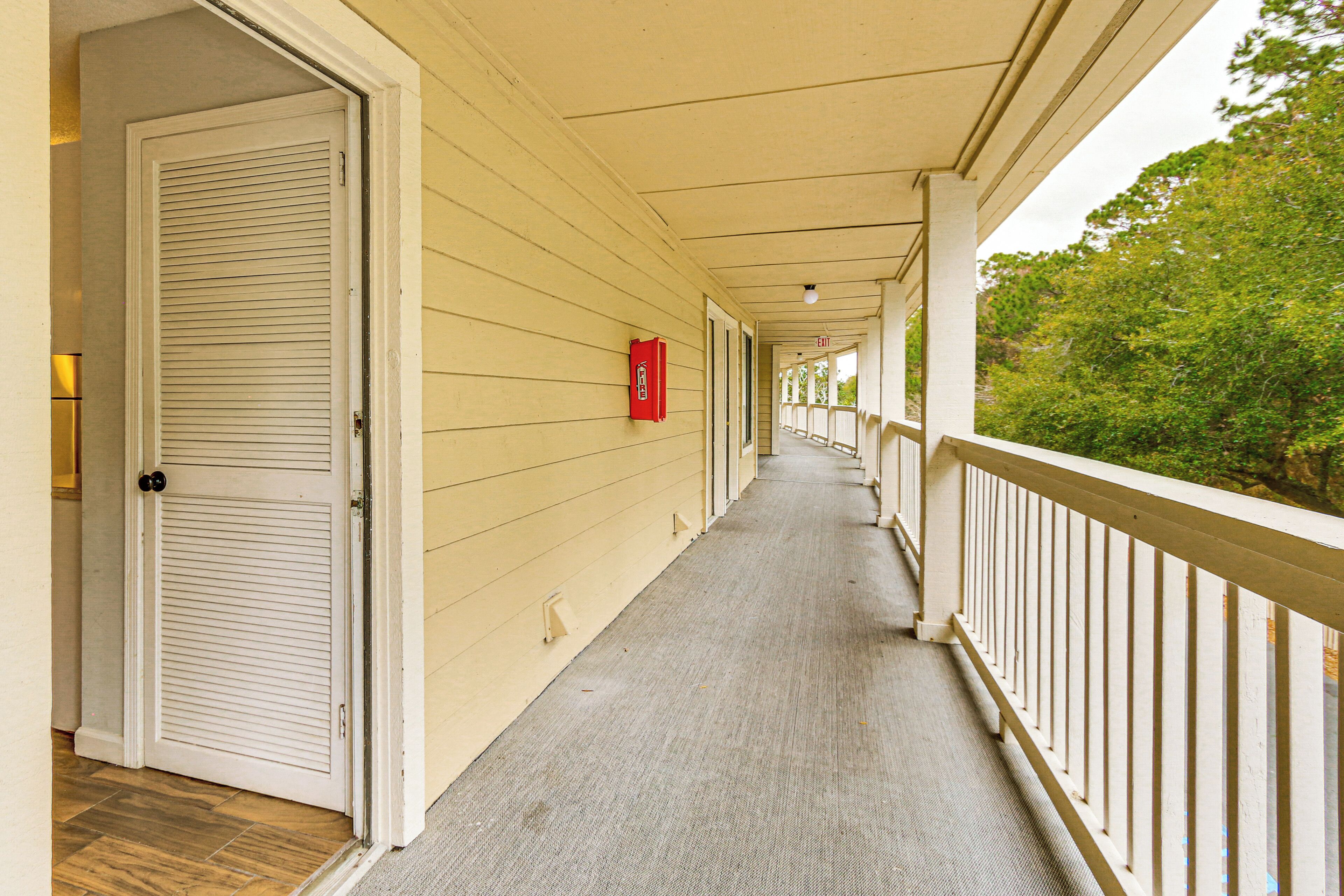 A covered corridor with a wooden floor, white walls, and a railing on one side.