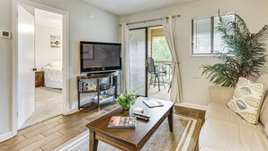 Een woonkamer met een flatscreen televisie, een salontafel, een bank, een potplant en een schuifdeur naar een balkon.