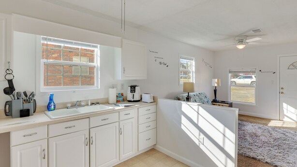 A kitchen with white cabinets, a large window, and a door leading outside. - Spotless King Retreat Near Maxwell AFB (Prattville)