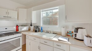 A modern kitchen with white cabinets, a built-in oven, a double sink, and a window providing natural light. - Spotless King Retreat Near Maxwell AFB (Prattville)