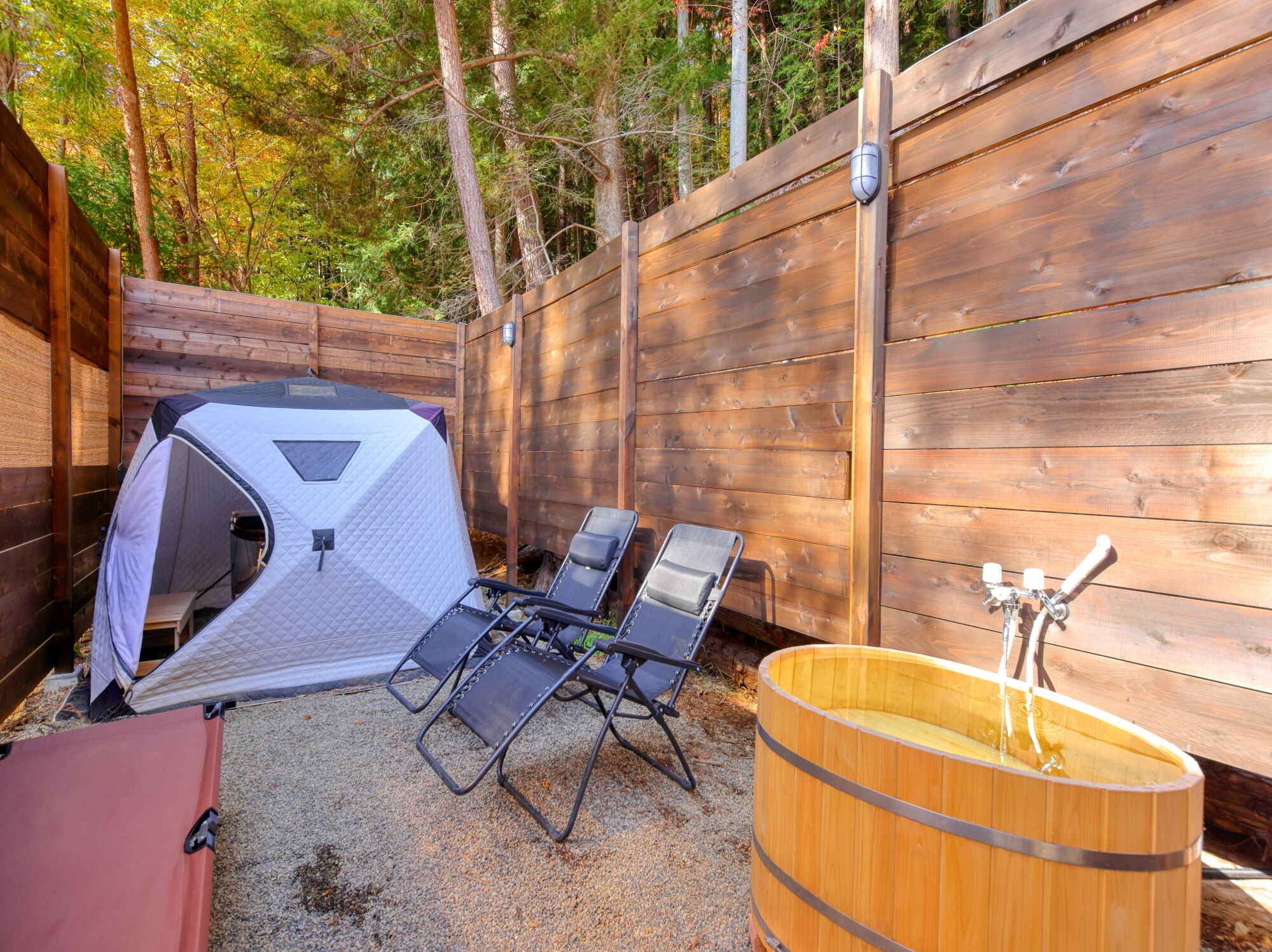 A camping area with a tent, two lawn chairs, a wooden barrel, and a wooden fence.