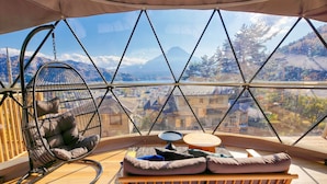 A cozy room with a hanging chair, a cushioned bench, and a small table, offering a panoramic view of a mountainous landscape. - Mt.Fuji Glamping Terrace MINENOHANA (Fujikawaguchiko)