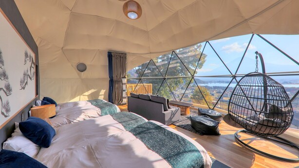 A cozy bedroom with a large bed, a sofa, and a hanging chair, featuring a scenic view through a large window. - Mt.Fuji Glamping Terrace MINENOHANA (Fujikawaguchiko)