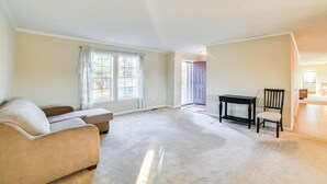 A spacious living room with a beige sofa, a small table, and a chair. There is a window with curtains and a door leading to another room. - Walk to Ohio River: Golconda Home w/ Water Views! (Golconda)