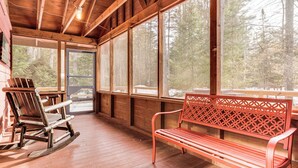 A wooden cabin interior with a rocking chair, a bench, and large windows offering a forest view. - Forested Retreat w/ Sauna: 5 Mi to Schroon Lake (Schroon Lake)