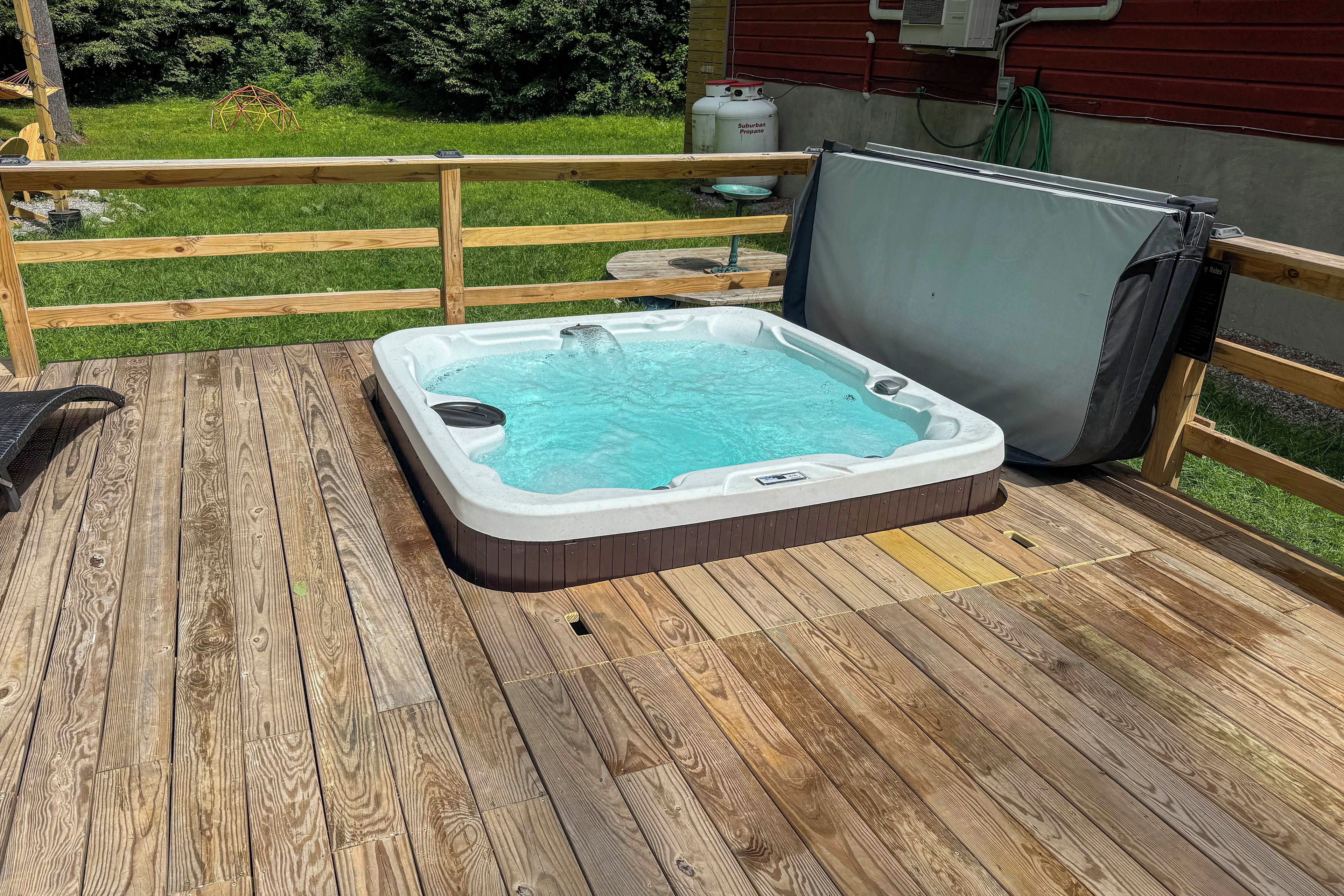 Un jacuzzi en una terraza de madera con un cerco de madera y un tanque de propano al fondo.