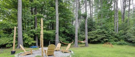 A forested outdoor area with a wooden deck, chairs, and hammocks.