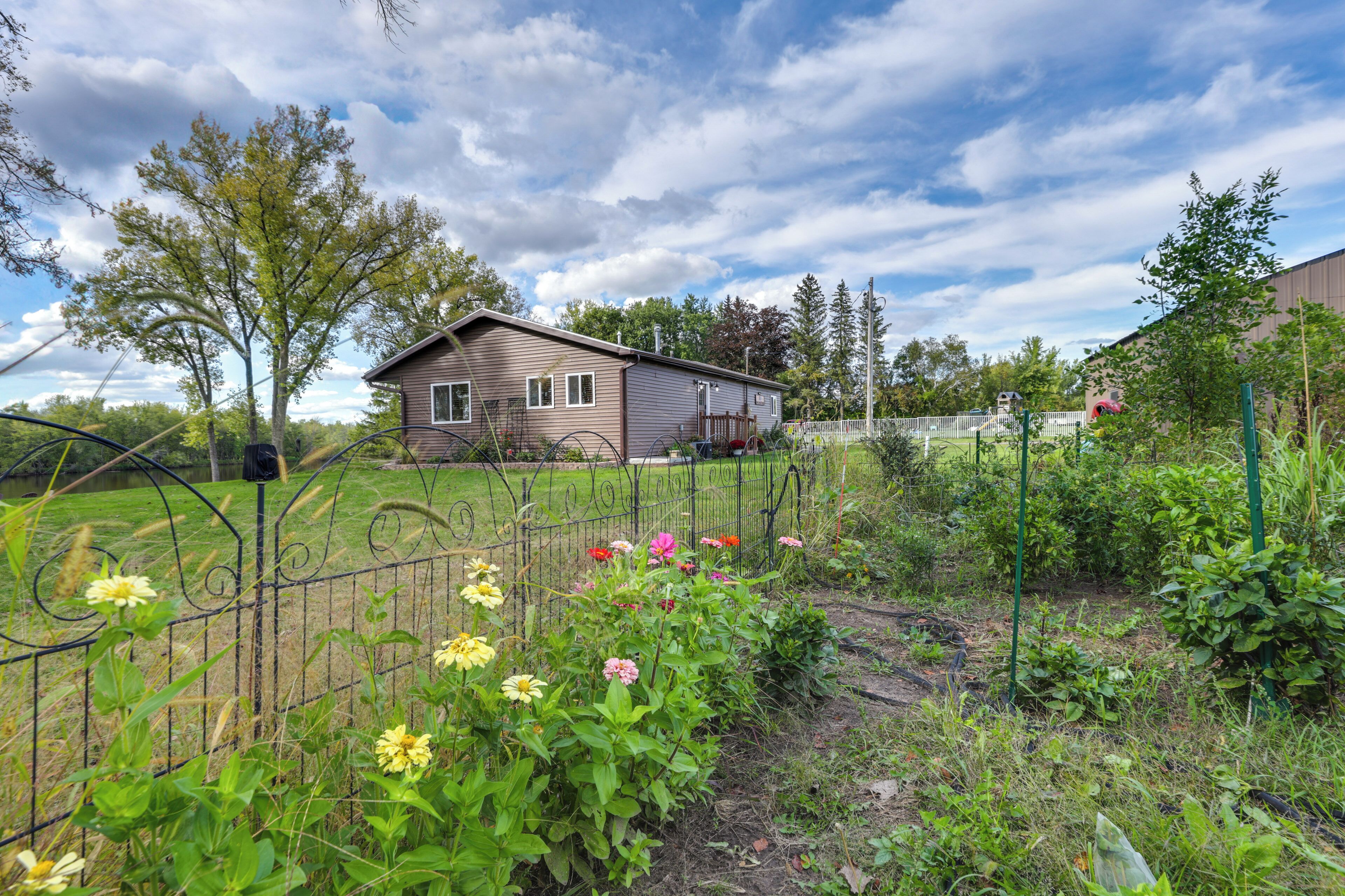 A single-story house with a front yard, surrounded by a metal fence and various plants.