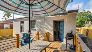 Une terrasse avec un parasol à rayures, une table en bois, une chaise bleue et un barbecue.