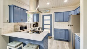 Een keuken met blauwe kastjes, een wit eiland, roestvrijstalen apparatuur en een houten plafond.