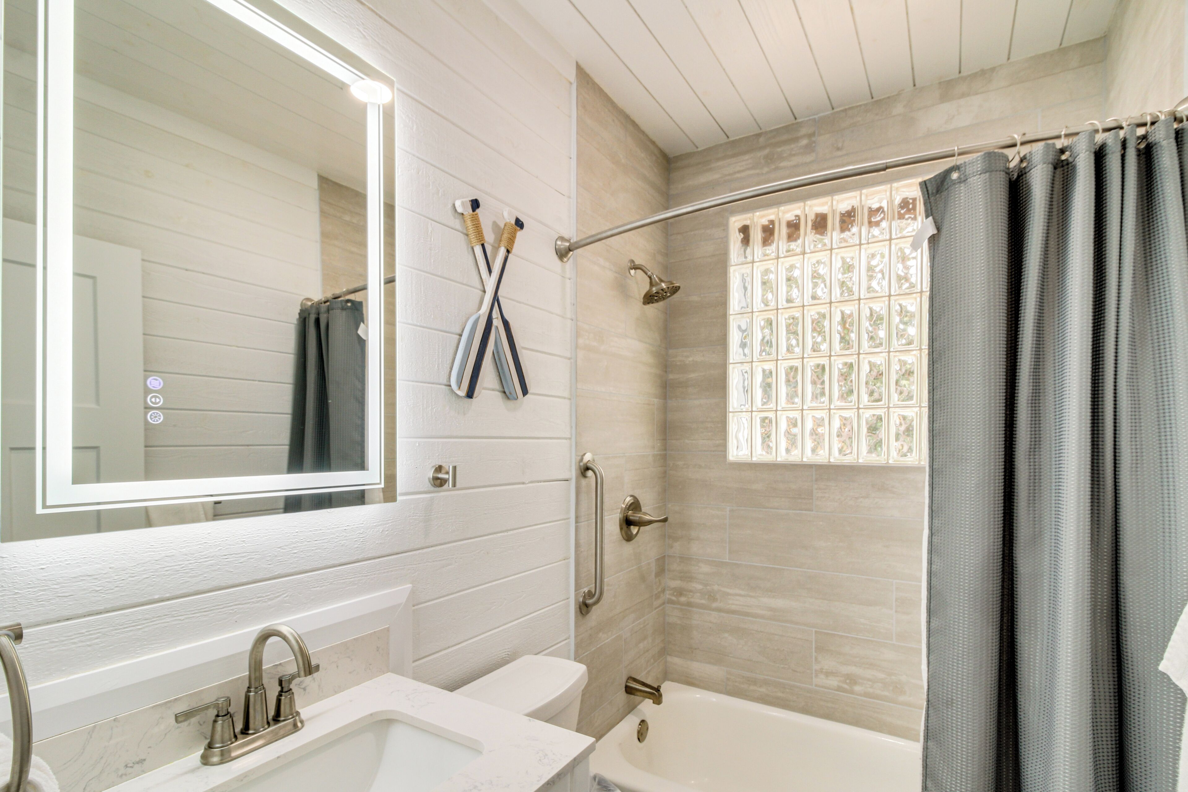 Une salle de bain avec un lavabo blanc, une baignoire, une douche avec une porte en verre et un miroir au-dessus du lavabo.