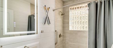 Une salle de bain avec un lavabo blanc, une baignoire, une douche avec une porte en verre et un miroir au-dessus du lavabo.