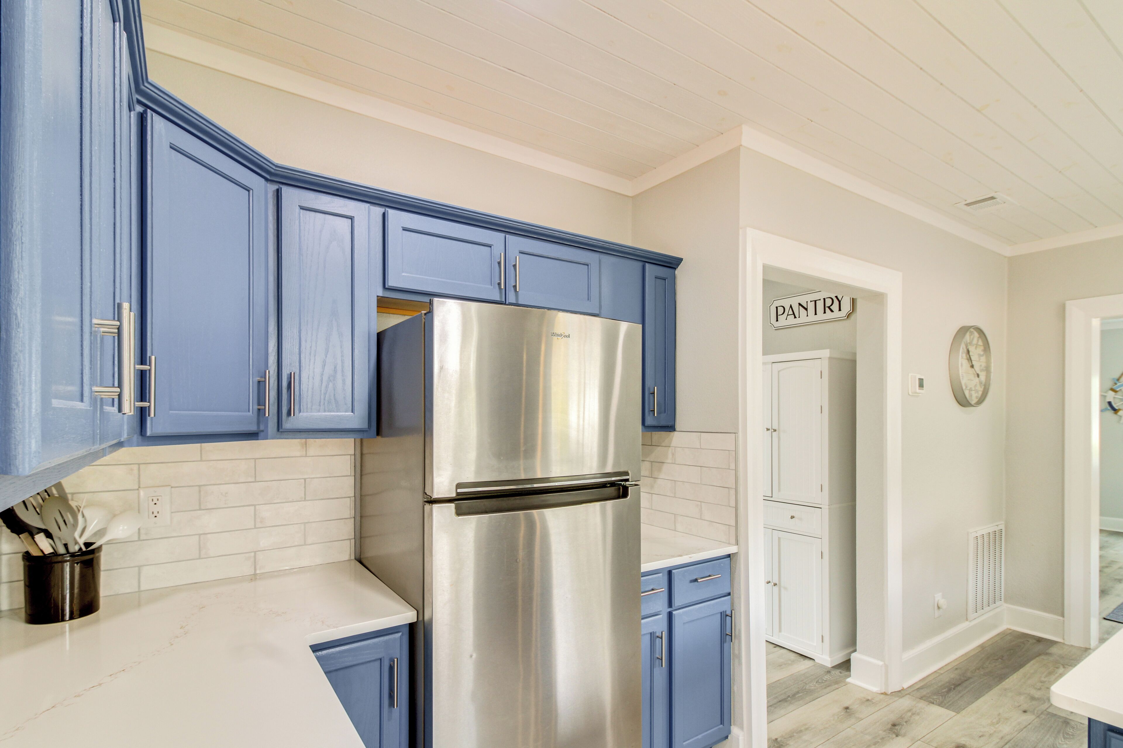 A kitchen with blue cabinets, a stainless steel refrigerator, and a white countertop.