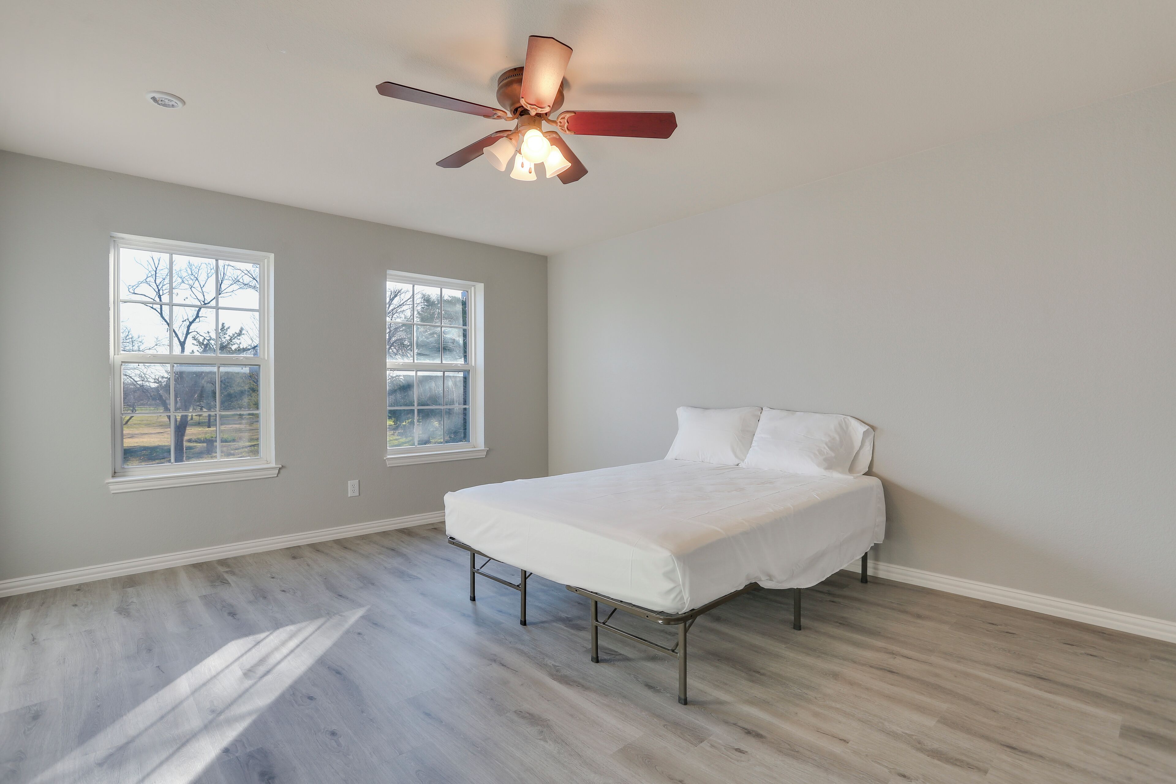 A bedroom with a bed, two windows, a ceiling fan, and a light fixture.