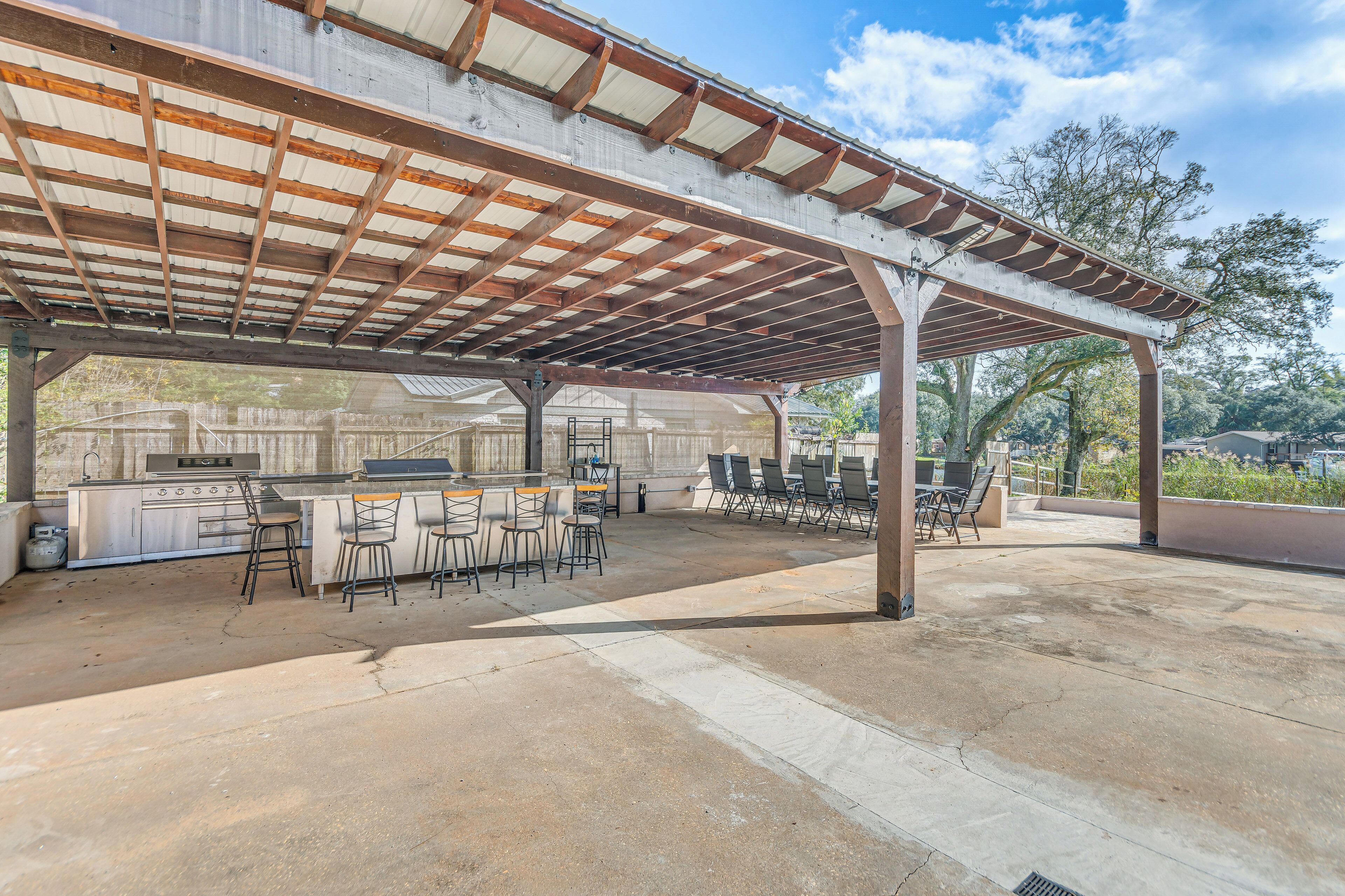 Un patio al aire libre con una parrilla y zona de bar, cubierto por un techo metálico y rodeado de sillas y mesas.