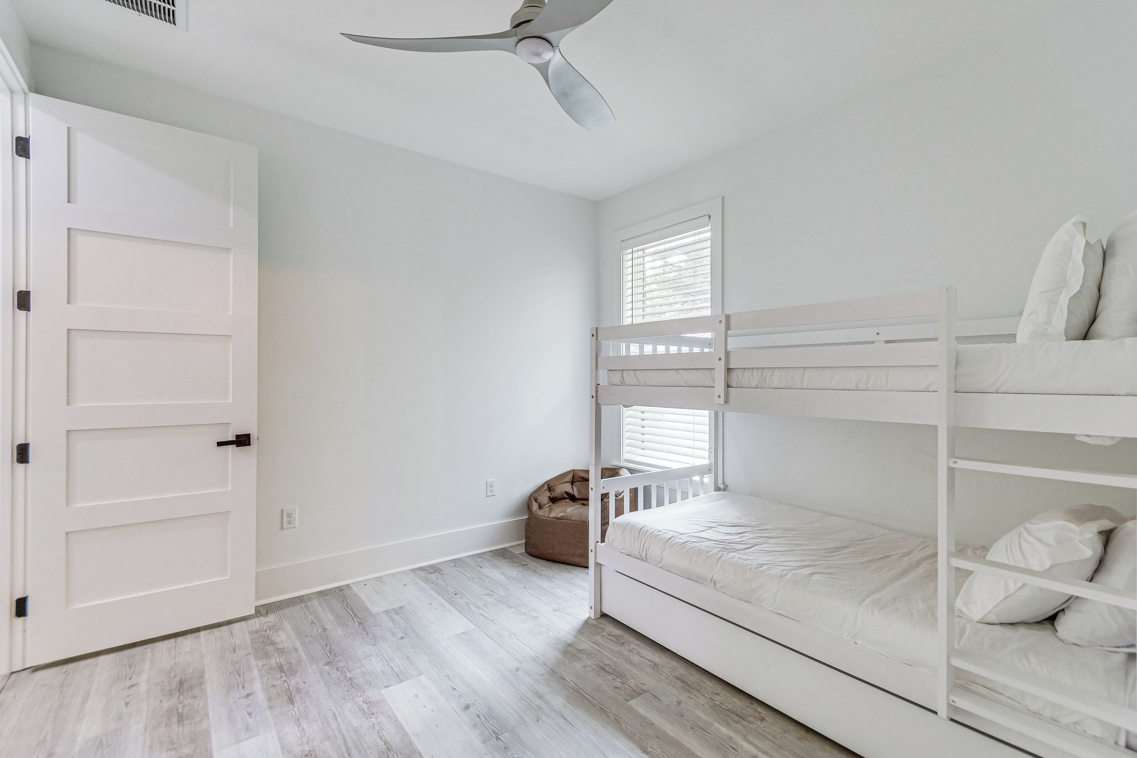 A room with a white door, a ceiling fan, a bunk bed, and a bean bag chair.