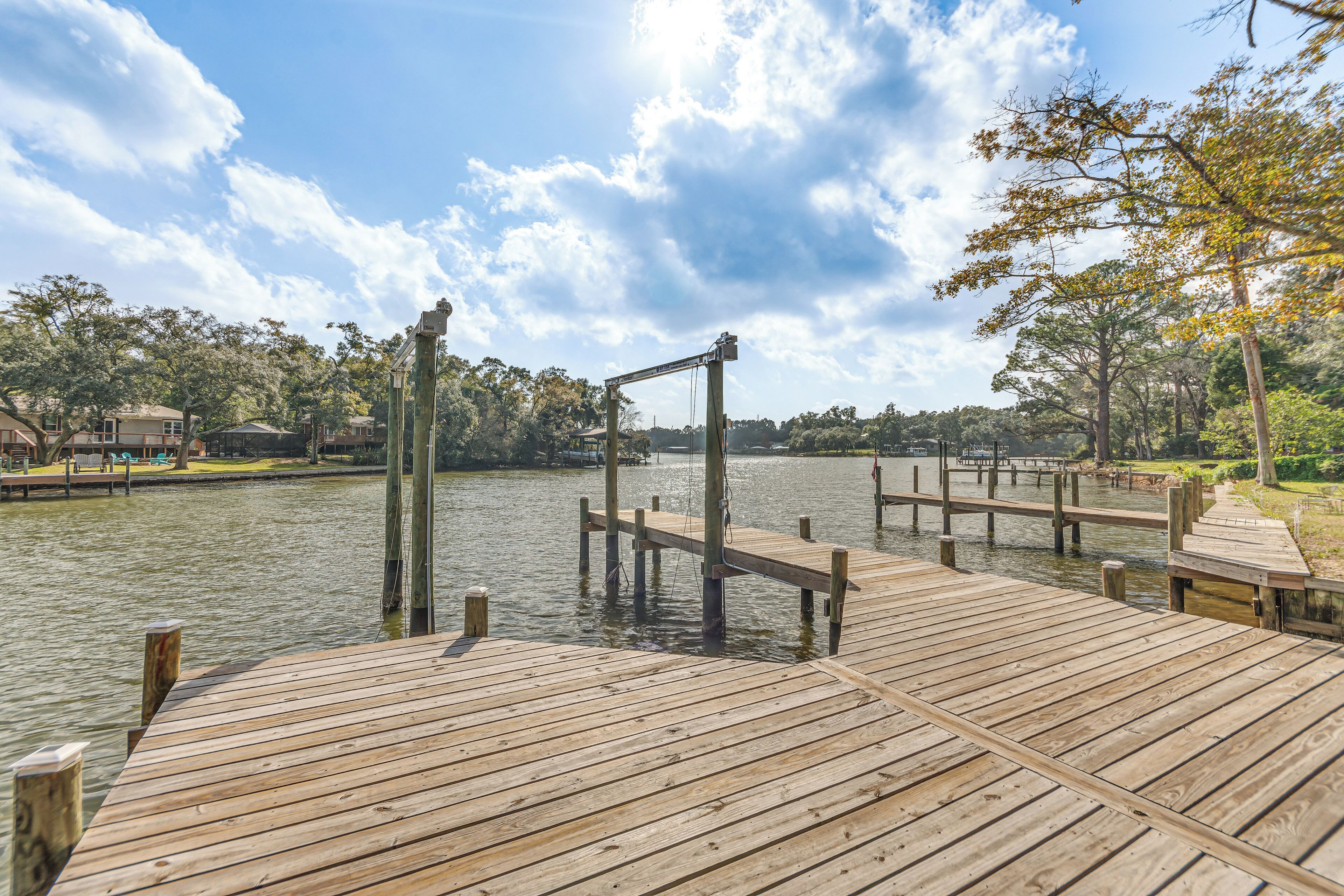 A wooden dock extending into a calm lake, surrounded by trees and a clear sky.