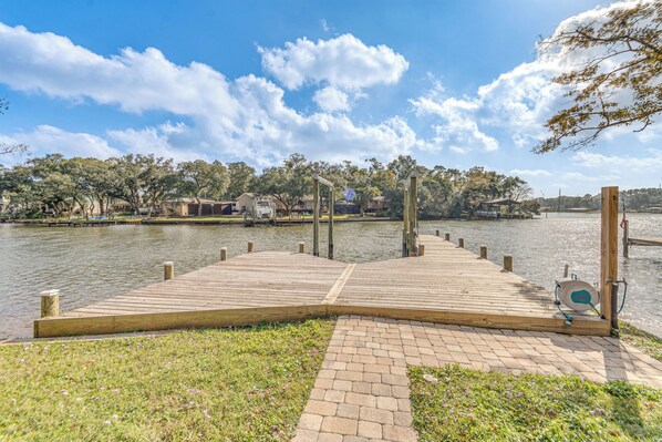 A wooden dock extending into a calm body of water, surrounded by grassy areas and trees.