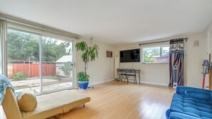 A spacious living room with a large sliding glass door, a blue sofa, a beige bench, a television, and a potted plant.