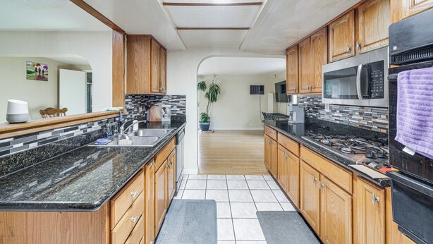 A modern kitchen with wooden cabinets, a granite countertop, stainless steel appliances, and a tiled floor.