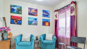 A room with two blue armchairs, a small table, a guitar, and six paintings on the wall.