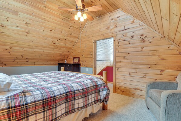 A bedroom with a plaid bedspread, a wooden ceiling fan, and a window with blinds.