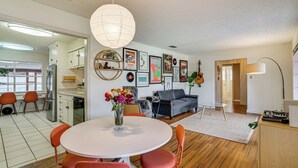 A modern kitchen with white cabinets, a dining table with orange chairs, and a large white pendant light. - Karaoke Ready! Fort Worth Area Home (Aledo)