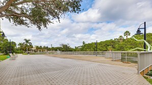 Un sendero pavimentado con bancos, una barandilla y vistas a un parque con árboles y un edificio al fondo.