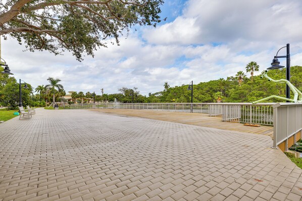 A paved walkway with benches, a railing, and a view of a park with trees and a building in the background.