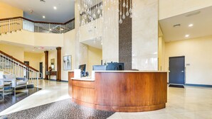 Un vestíbulo amplio con mostrador de recepción, una escalera y un alto techo con luces colgantes.