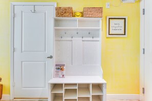 A white storage unit with baskets and hooks, a framed inspirational quote, and a small table with a brochure.