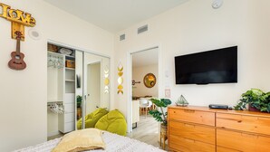 Un dormitorio con cama, cómoda, televisor, guitarra y armario.
