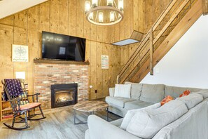 Una sala de estar acogedora con chimenea, un televisor de pantalla plana grande, un sofá cómodo y una escalera de madera.