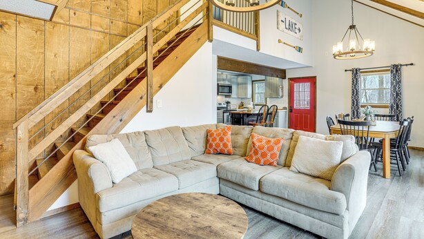 A spacious living area with a large L-shaped sectional sofa, a wooden staircase, and a dining area with a red door. - Walk to Hideout Slopes: Home w/ Game Room! (Lake Ariel)
