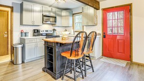 A kitchen with a central island, wooden chairs, a red door, and a stainless steel trash can. - Walk to Hideout Slopes: Home w/ Game Room! (Lake Ariel)