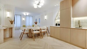 Une cuisine moderne avec des meubles en bois, un coin repas doté d’une table et de chaises blanches, et un luminaire au plafond.