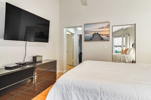 A hotel room with a large bed, a flat-screen TV mounted on the wall, a dresser, and a painting of a sunset.
