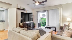 Ein Wohnzimmer mit Flachbildfernseher, Deckenventilator, Sofa, Couchtisch und Essbereich mit Tisch und Stühlen.