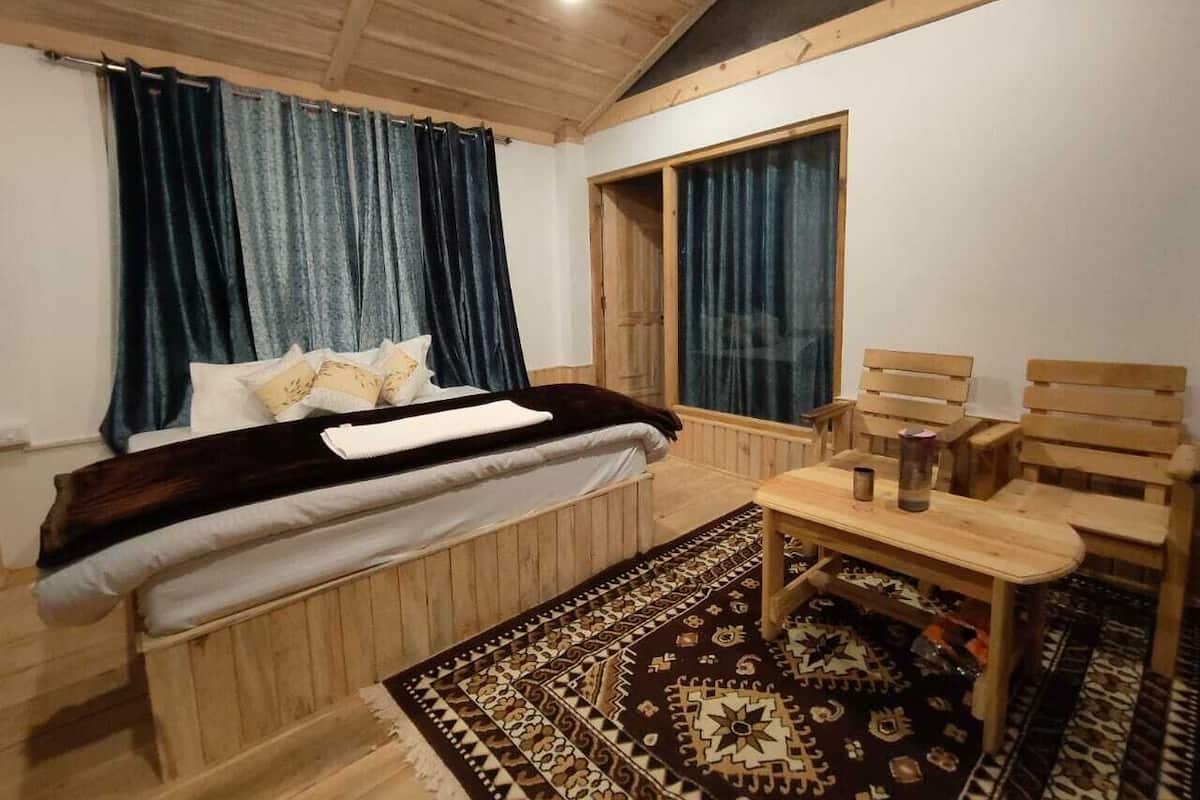 Et soveværelse med en seng, et træhovedgærde, et lille bord med stole, en tæppe med mønster og et vindue med gardiner.