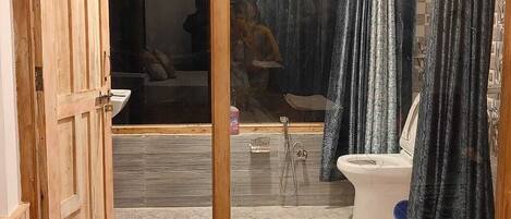 A bathroom with a wooden door, a shower, a toilet, and a mirror.