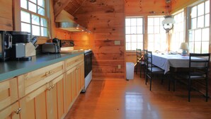 A wooden cabin interior with a kitchen and dining area, featuring wooden cabinets, a stove, and a dining table with chairs. - Unique Coastal Retreat in Exclusive Condo Complex (2392) (Truro)