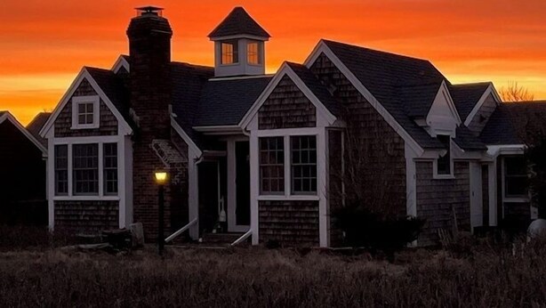 A row of houses with a prominent chimney and a small tower-like structure, set against a sunset sky. - Unique Coastal Retreat in Exclusive Condo Complex (2392) (Truro)