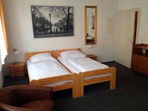 A room with a double bed, a chair, a desk, a mirror, and a painting on the wall.