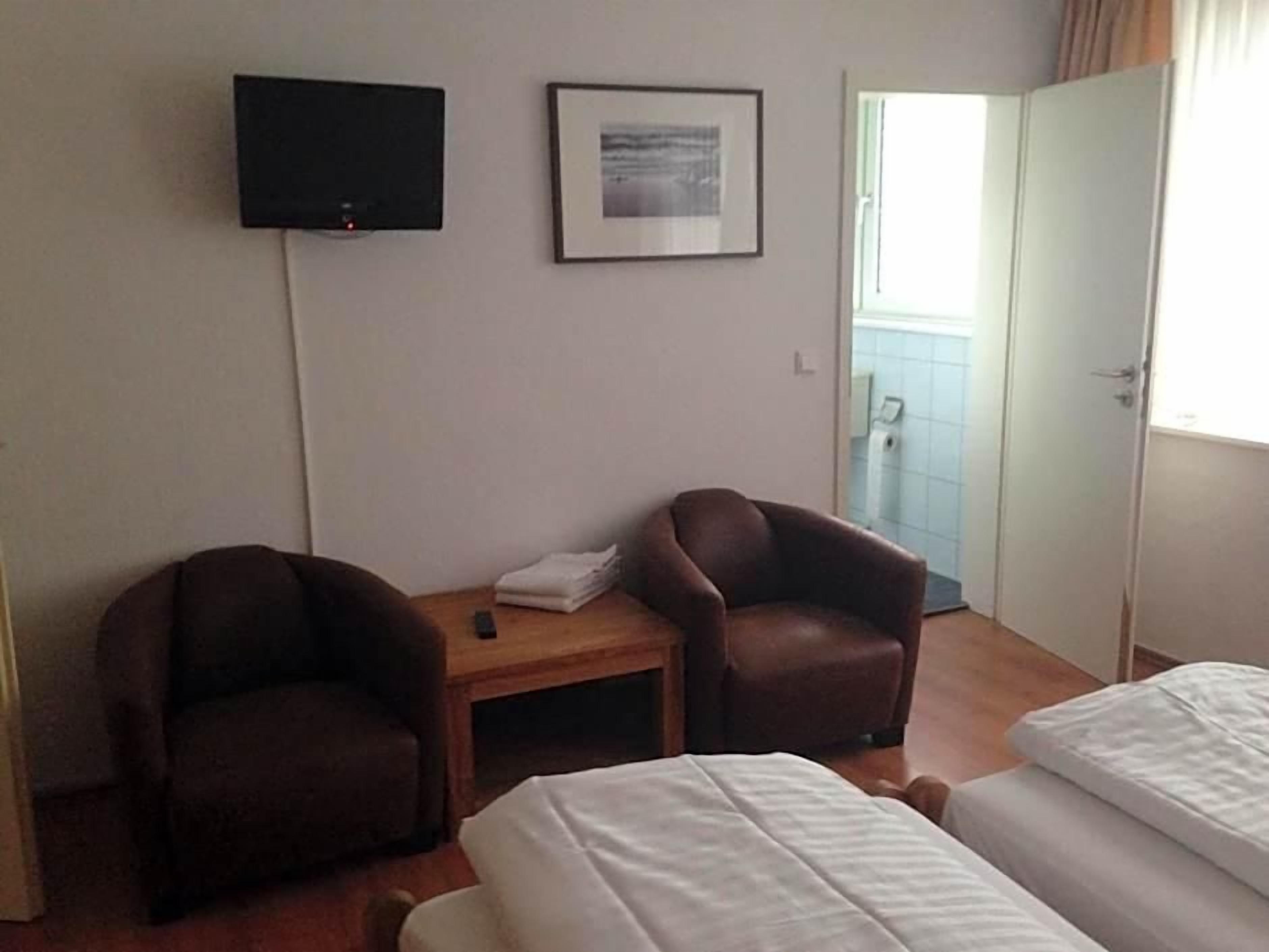Een hotelkamer met twee eenpersoonsbedden, een aan de muur bevestigde televisie, een lijst met een afbeelding en een deur naar een balkon.