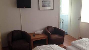Een hotelkamer met twee eenpersoonsbedden, een aan de muur bevestigde televisie, een lijst met een afbeelding en een deur naar een balkon.