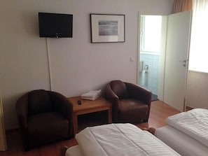 A hotel room with two single beds, a TV mounted on the wall, a framed picture, and a door leading to a balcony.