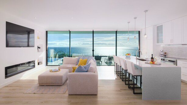 A modern kitchen with a large island, a dining area with a view of the sea, and a cozy seating area with a sofa and cushions.